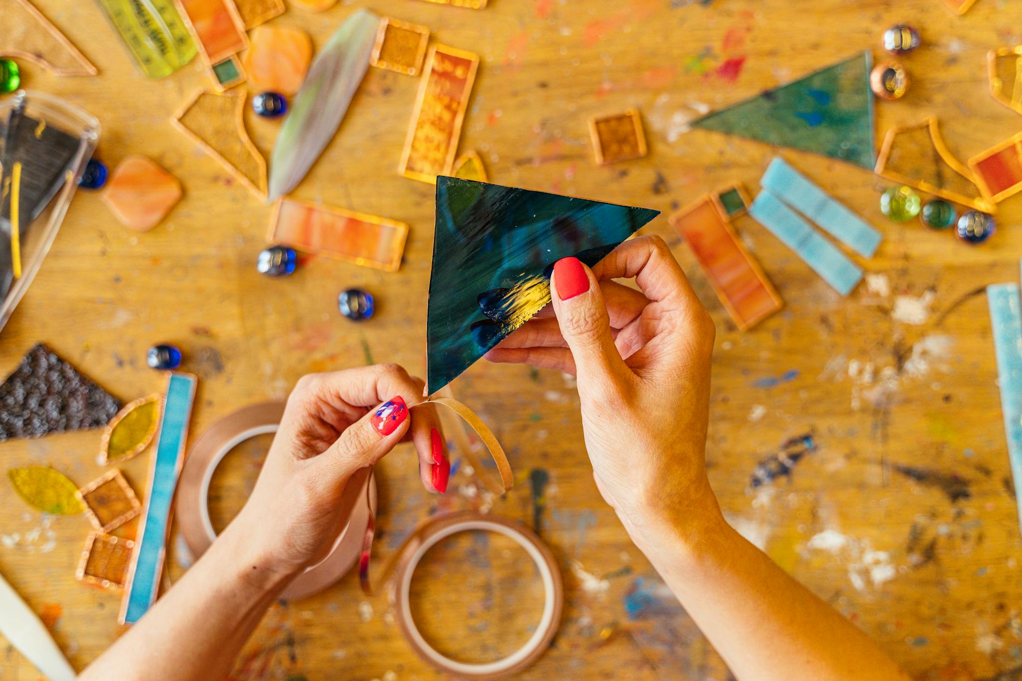 Hands crafting stained glass art with colorful pieces on a wooden table.