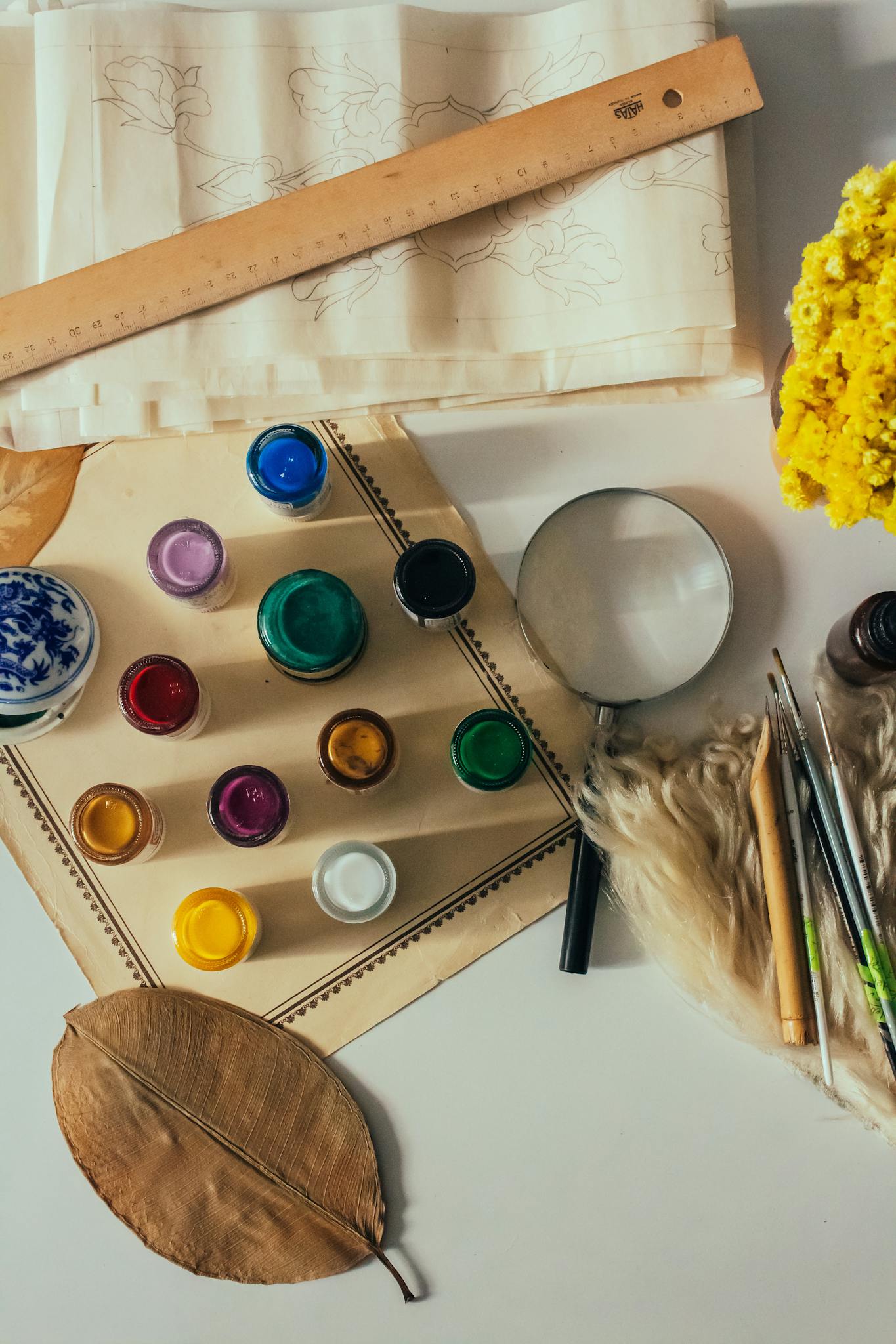 Top view of art supplies including paints, brushes, and flowers, ideal for creative projects.