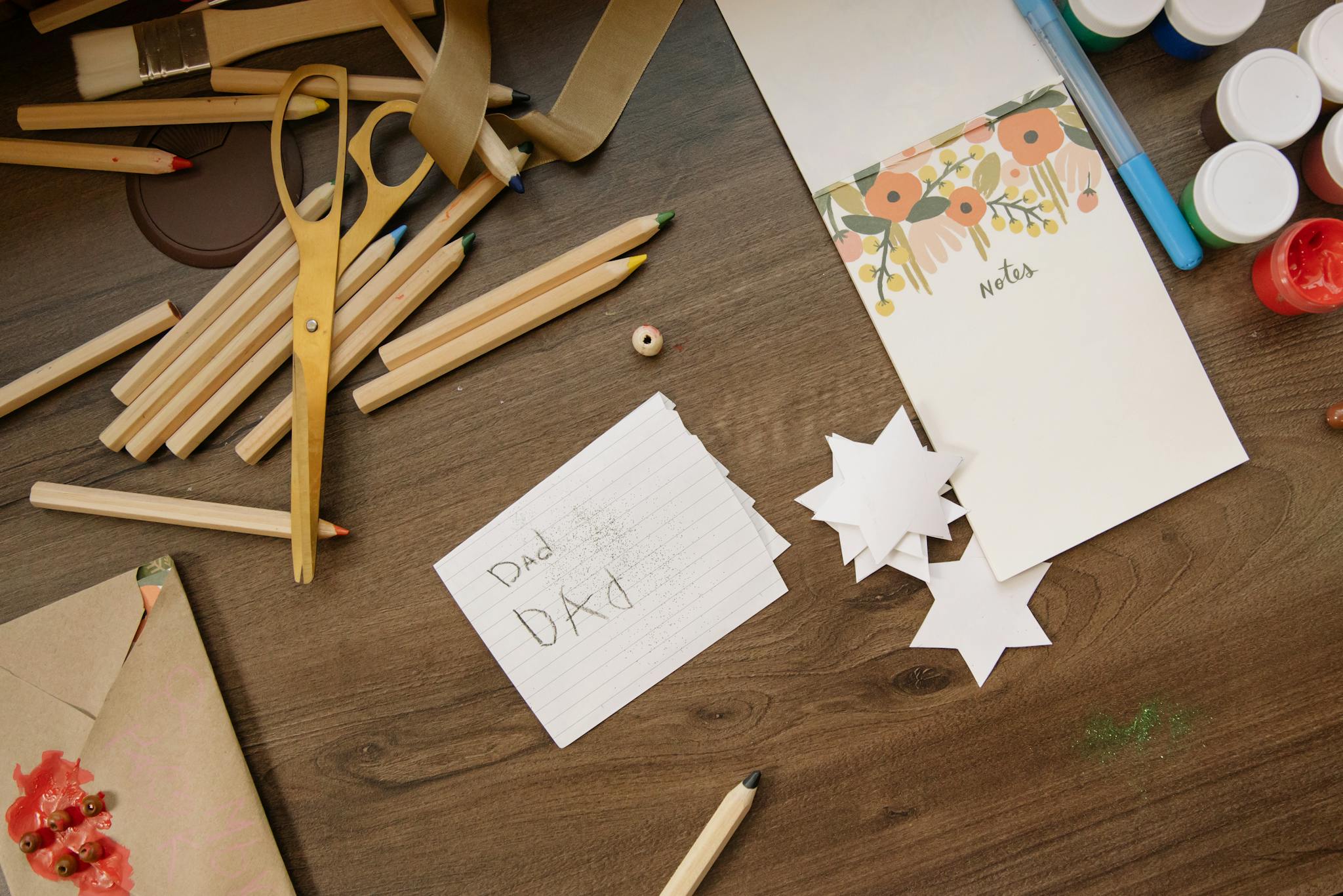 Top view of art supplies including scissors, pencils, and handmade stars on a wooden surface.
